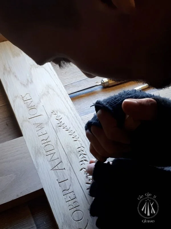 Welsh, Gloran wood carver Cân Cŷn y Gloran, carving decorative leaves and the words Robert Andrew Jones into an oak cross by hand with a sharp chisel.