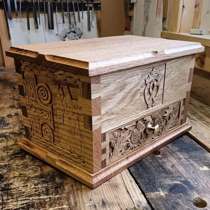 An oak chest, filled with custom carvings of various Scottish symbols, with a front draw with a brass knob.