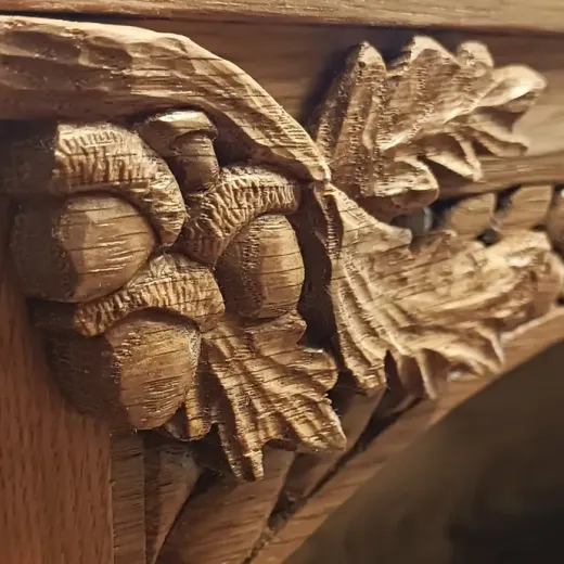The top of an oak cabinet, with oak carved leaves and acorns, with handcarved celtic knotwork in the background