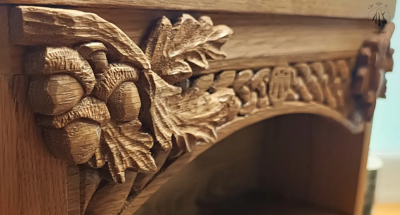 The top of an oak cabinet, with oak carved leaves and acorns, with handcarved celtic knotwork in the background