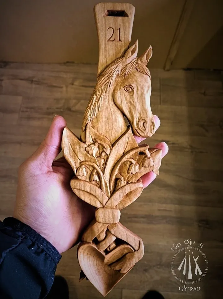 A hand carved cherry lovespoon, featuring a horse, lily of the valley, and ribbons, for a 21st birthday, carved by Arwyn of Cân Cŷn y Gloran